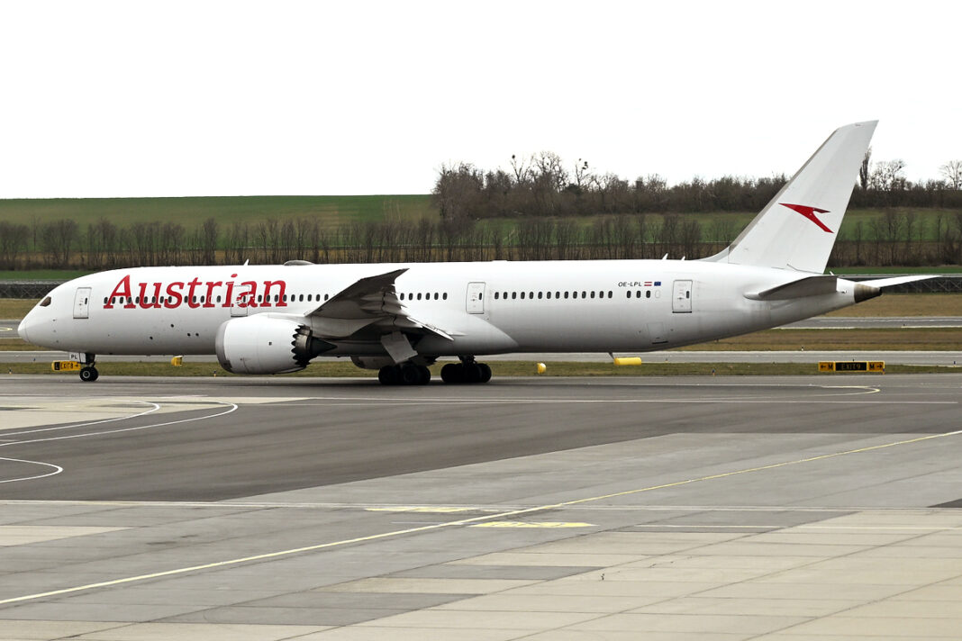 Austrian lieta nad Saudskou Arábiou, Swiss sa jej vyhýba Boeing 787-9 v červeno-bielych farbách Austrian Airlines roluje po letiskovej ploche pod zamračenou oblohou.