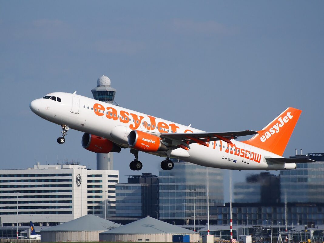 easyJet ruší ďalších 700 000 sedadiel, dôvod je v nádrži Airbus A320 spoločnosti easyJet krátko po vzlete, pohľad zboku spod stúpajúceho lietadla s vysunutými vztlakovými klapkami
