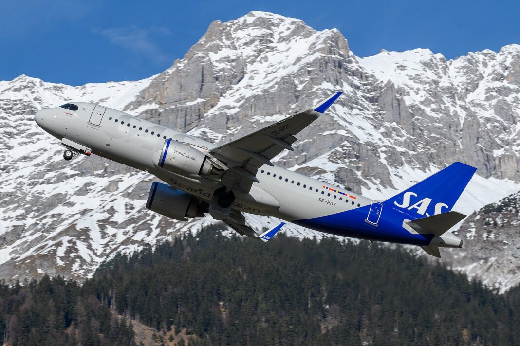 Rýchle Wi-Fi na palube prestáva byť výsadou biznis triedy Airbus A320neo spoločnosti SAS Scandinavian Airlines stúpa po štarte nad zasneženými horami, pohľad zdola zozadu na modrý chvost s logom SAS.
