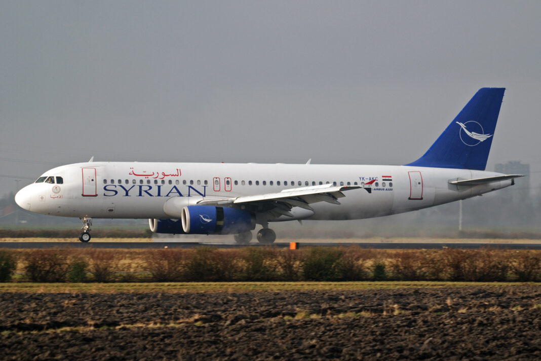 Airbus A320 spoločnosti Syrian Air tesne nad dráhou, v pozadí poľná krajina a zamračená obloha.