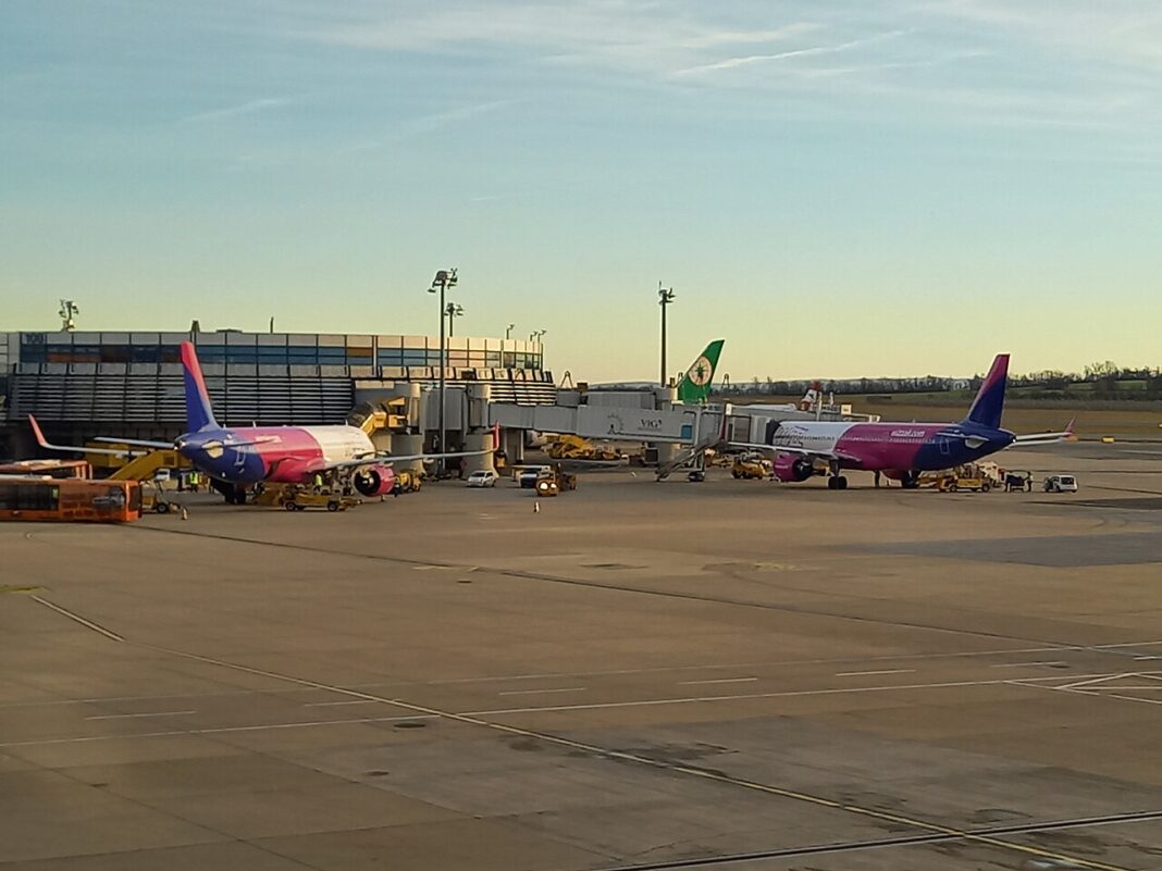 Wizz Air pribral 24 % cestujúcich, Ryanair len štyri percentá Dve lietadlá Wizz Air stoja pri nástupných mostoch terminálu, okolo nich technika pozemného odbavenia, denné svetlo