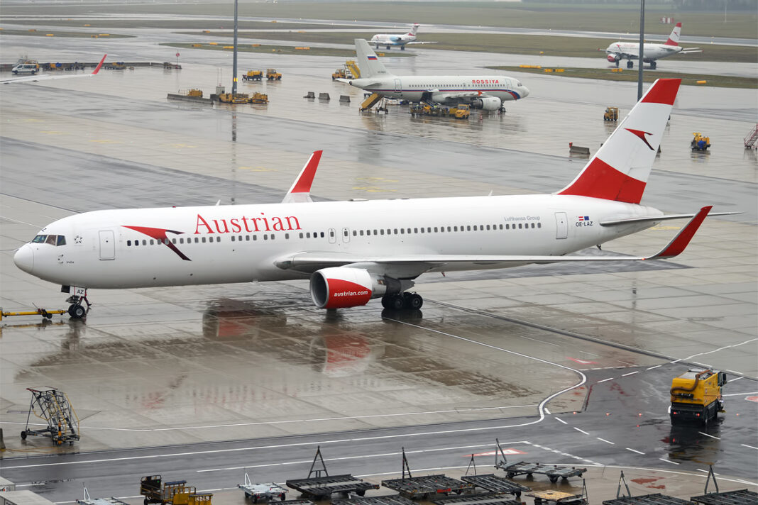 Boeing 767-300ER v červeno-bielych farbách Austrian Airlines roluje po mokrej letiskovej ploche.