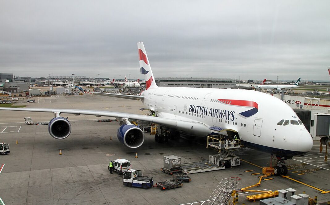 Menšie lietadlo, najväčšia biznis trieda. British Airways mení A380 Dvojpodlažné lietadlo Airbus A380 v nátere British Airways stojí pri prstovom nástupišti, okolo neho obslužná technika a kontajnery s batožinou.