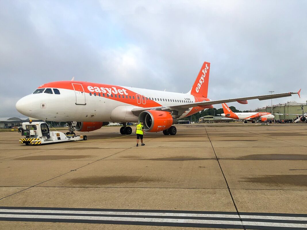 Lietadlo easyJet pri odtláčaní od terminálu, pred ním stojí pracovník pozemnej obsluhy a ťahač.