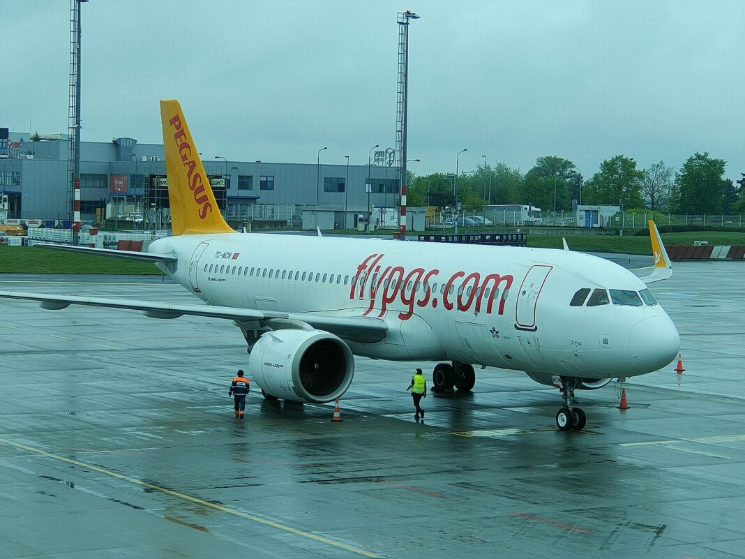 Pegasus zaplatil za Smartwings a ČSA 154 miliónov eur Airbus A320 spoločnosti Pegasus Airlines s nápisom flypgs.com na trupe stojí na mokrej odbavovacej ploche letiska, pri prednej časti pracujú dvaja zamestnanci pozemnej obsluhy v reflexných vestách.