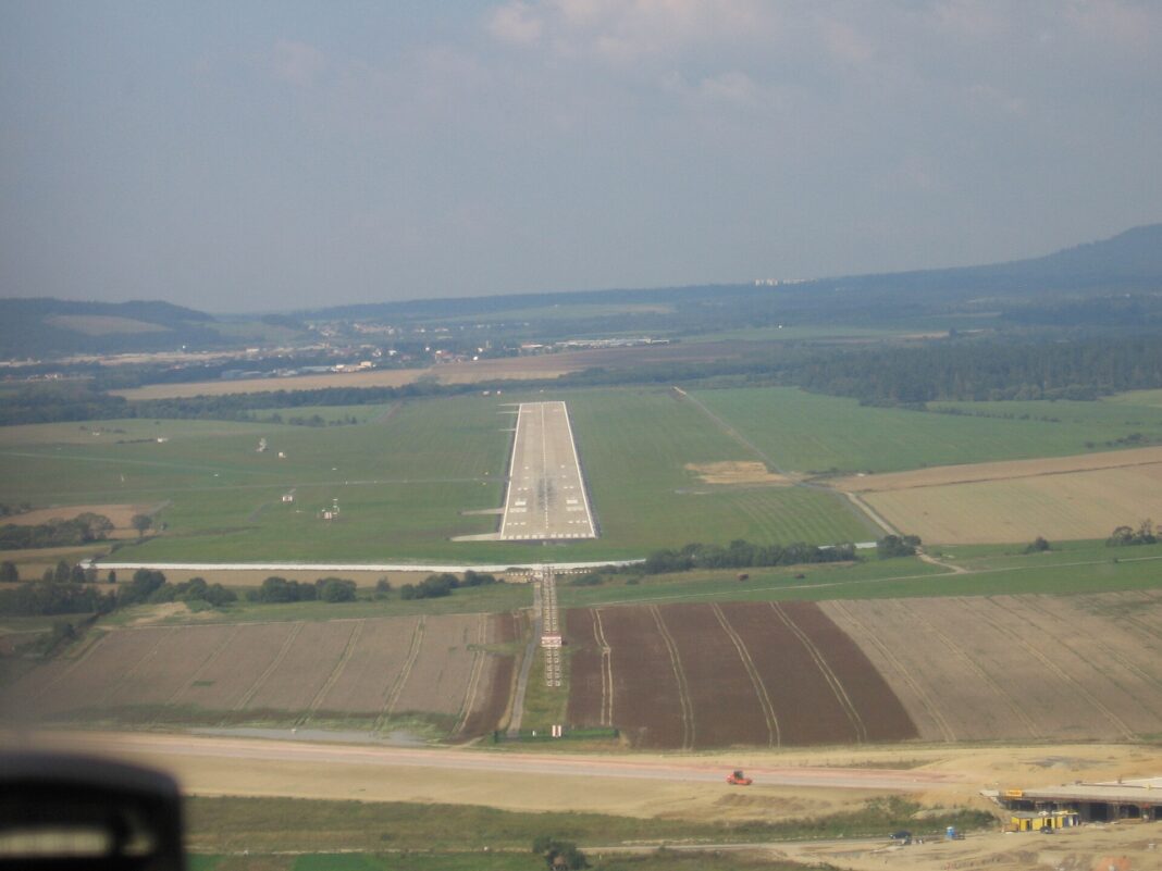 Linka Praha – Poprad s Wizz Air trvá hodinu, vlak takmer sedem Pristávacia dráha letiska Poprad-Tatry pri pohľade z klesajúceho lietadla, okolo nej polia a v pozadí kopce.